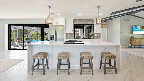 Een moderne keuken met een groot eiland, barkrukken en hanglampen.