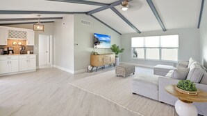 Een ruime woonkamer met een keuken, een groot raam en een plafond met zichtbare balken.