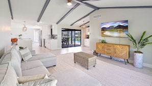 Een ruime woonkamer met een grote bank, een houten kast en een televisie waarop een mooi landschap te zien is.