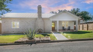 A single-story house with a stone facade, a chimney, and a front porch with two chairs.