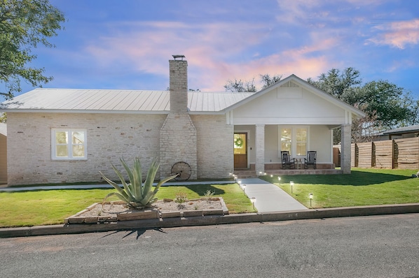 A single-story house with a stone facade, a chimney, and a front porch with two chairs.