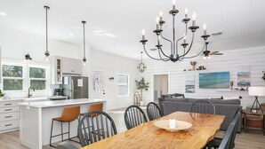 A modern kitchen with white cabinetry, a central island with bar stools, and a dining table with chairs.