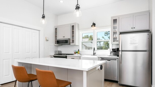 A modern kitchen with white cabinetry, stainless steel appliances, and a central island with two bar stools.