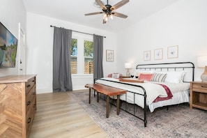 A bedroom with a bed, bedside tables, a wooden dresser, a ceiling fan, and a window with curtains.