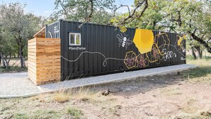 A black container with a wooden structure on one side, a window, and a mural with bee and honeycomb designs.