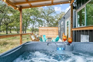 A hot tub with two drinks, wooden deck, and outdoor seating.