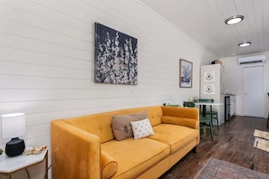 Una sala de estar con un sofá amarillo, una mesa con una lámpara y un cuadro en la pared.