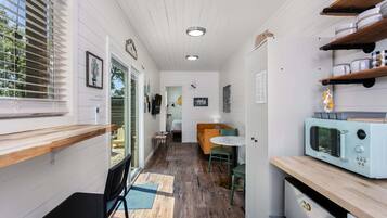 A compact kitchen with a microwave, wooden shelves, and a dining area with a table and chairs.
