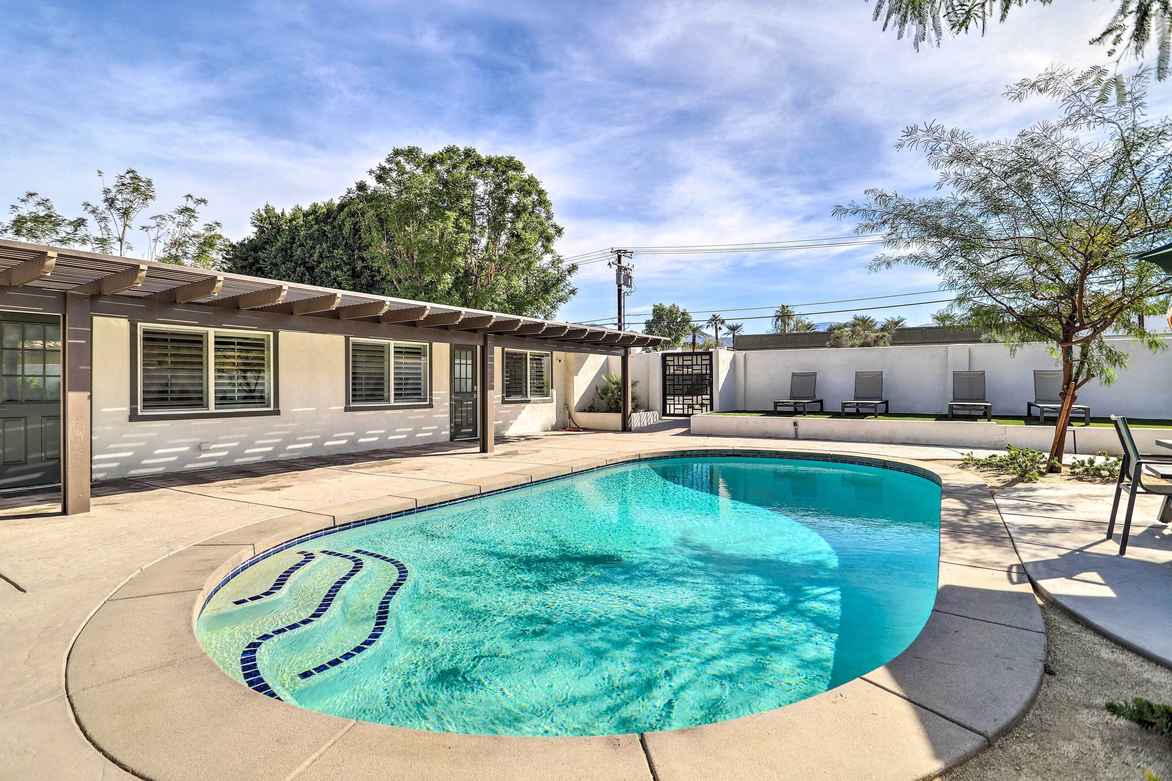 A swimming pool with a curved edge, surrounded by a patio area with chairs and a pergola.