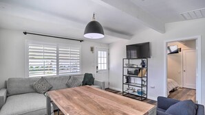 A modern living room with a wooden dining table, grey sofa, and a TV mounted on the wall. - Walk to Downtown Palm Desert: Home w/ Pool Access (Palm Desert)