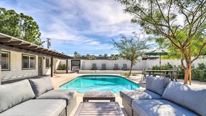 A poolside area with a built-in sofa and a wooden table, surrounded by a white wall and trees. - Walk to Downtown Palm Desert: Home w/ Pool Access (Palm Desert)