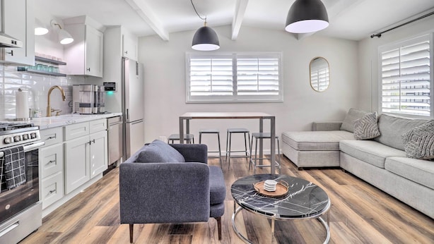 A modern kitchen with white cabinets, a stove, and a dining area with a table and chairs. - Walk to Downtown Palm Desert: Home w/ Pool Access (Palm Desert)
