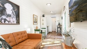 A cozy living room with a leather sofa, a coffee table, and a rug. There is a kitchen area with a sink and cabinets, and a dining area with a chair. - Honey at the Hive, 1/1 | Private Hot Tub | Gas Fire Pit | Cornhole (Fredericksburg)