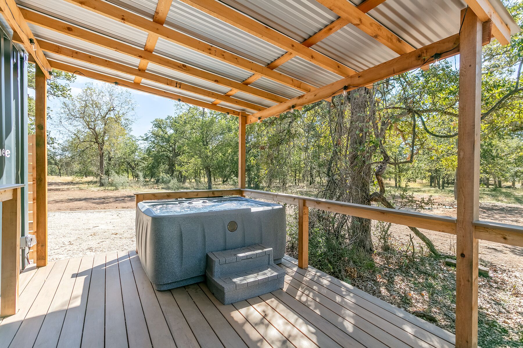 Ein Whirlpool auf einer Holzterrasse mit Metallveranda, umgeben von Bäumen.