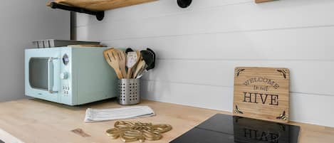 A kitchen with a vintage-style microwave, a wooden cutting board, a stainless steel utensil holder, and a welcome sign.