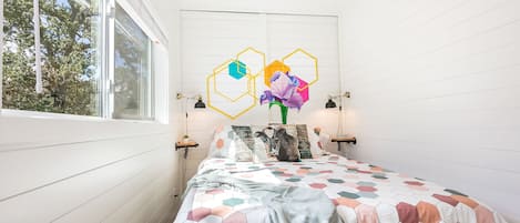 Un dormitorio con cama, ventilador de techo, ventana y pared con diseños geométricos.