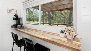 Une cuisine avec un coin café, un panneau indiquant « SAUVONS LES ABEILLES », et une vue sur les arbres à l’extérieur.