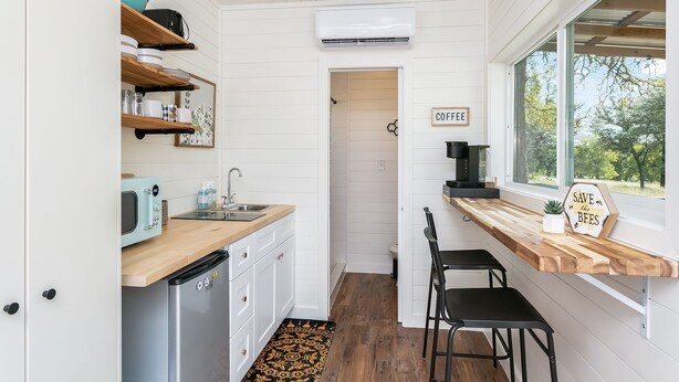 Une cuisine compacte avec des meubles blancs, un four à micro-ondes encastré, un coin café et une vue par la fenêtre.