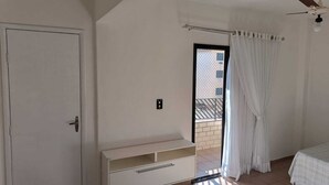 Ein Zimmer mit Tür, einem weißen Schrank, einem Deckenventilator, einem Fenster mit Vorhängen und einem Bett.