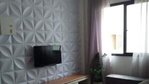 Ein Wohnzimmer mit Wandmuster, einem Flachbildfernseher, einer Couch, einem Couchtisch und einem Fenster mit Vorhängen.