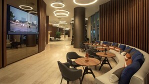 A modern lounge area with a large TV screen, circular ceiling lights, and a seating area with sofas and tables. - Amazing apartment Lyfe Resort-& Residences- Ocean view! (Hollywood)