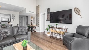 A modern living room with leather sofas, a glass coffee table, a flat-screen TV, and a dining area with a kitchen in the background. -  NEW & GORGEOUS Lakefront ZEN 3 bedrooms [2 KING +1 Queen] (Phoenix)