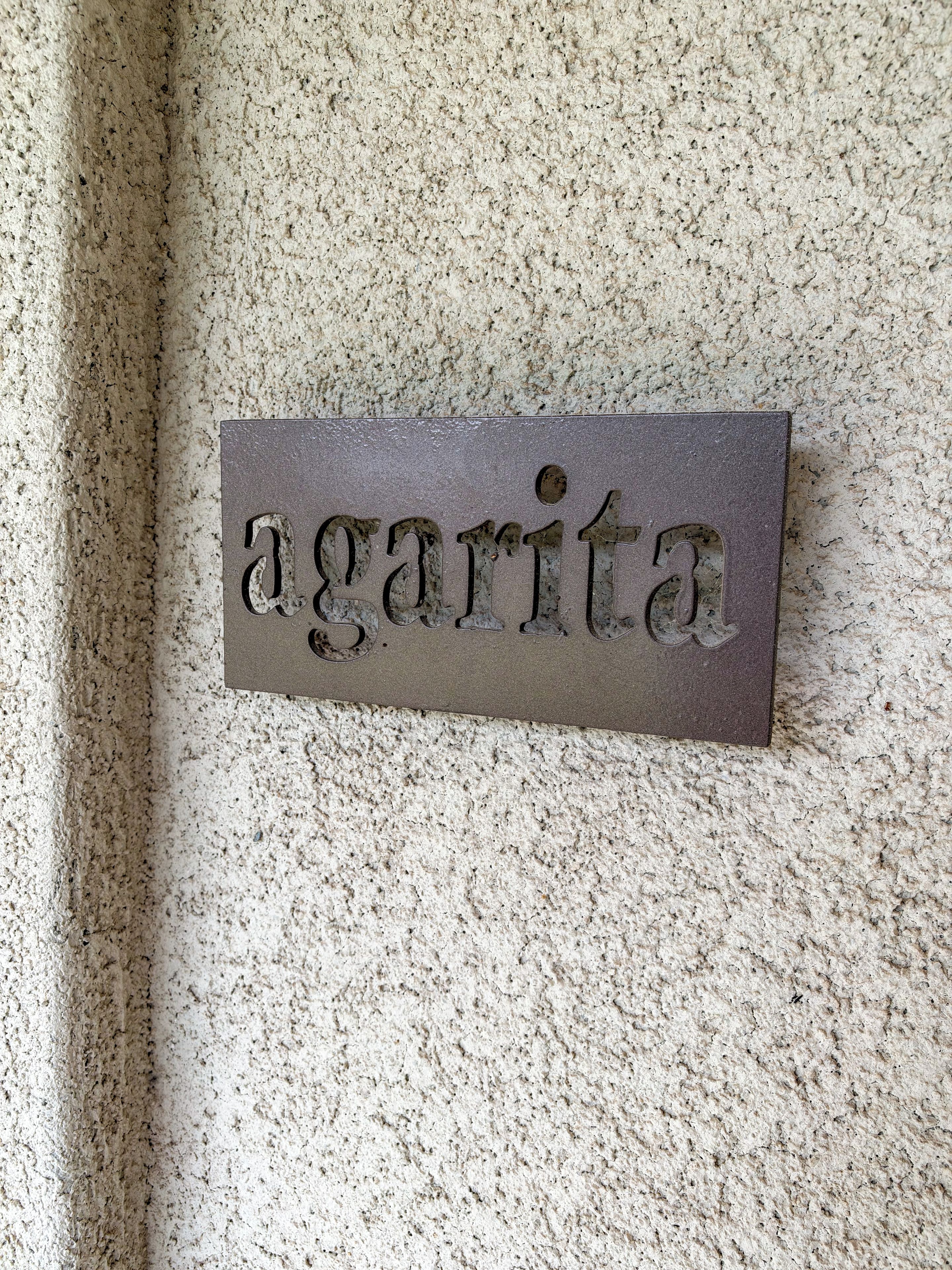 A metal plaque with the word 'agarita' mounted on a textured wall.