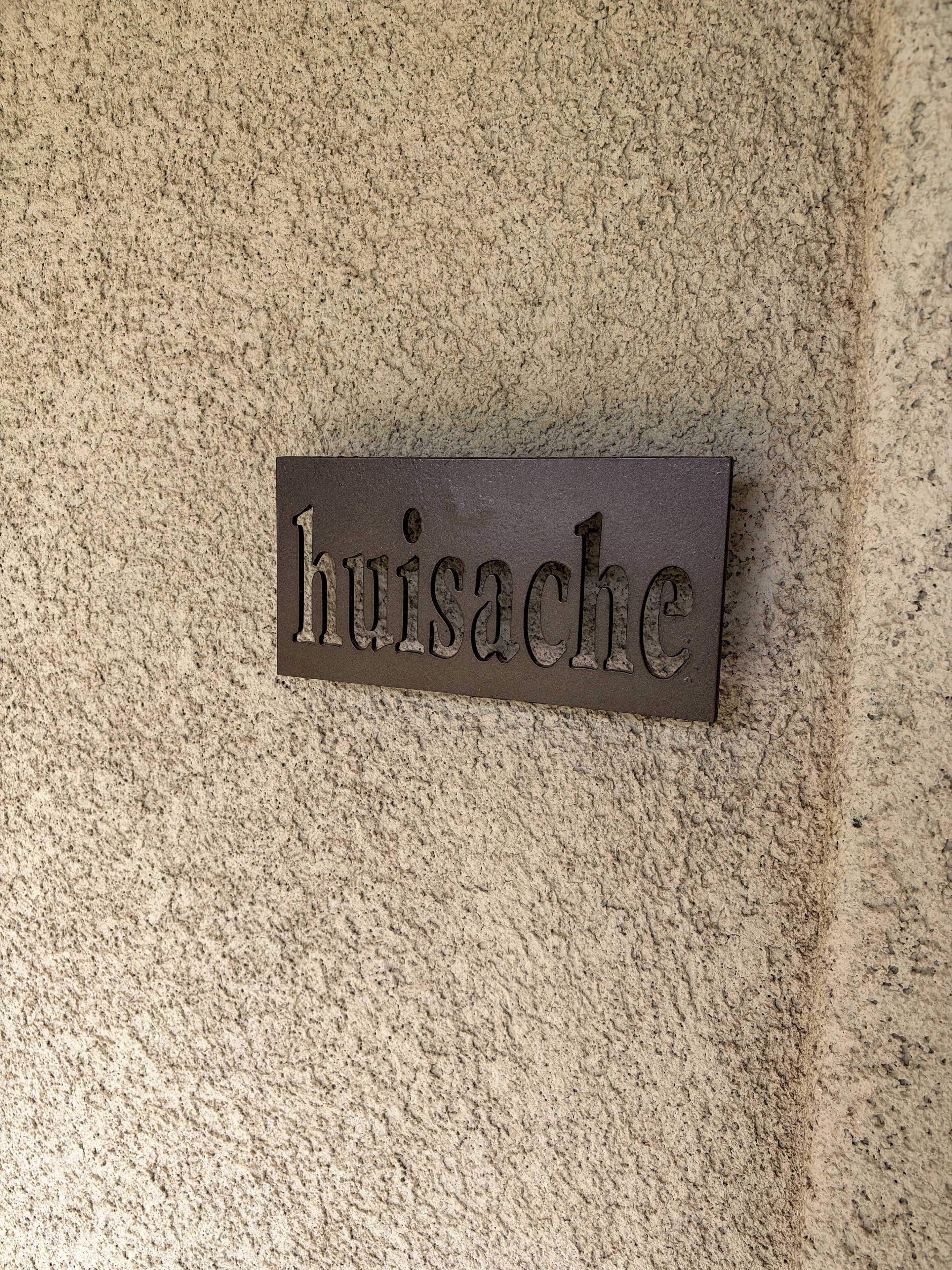 A metal plaque with the word 'huisache' on a textured wall.
