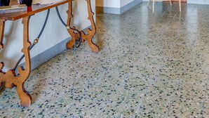 Un hall spacieux doté d’un sol en terrazzo poli, d’une console en bois sur laquelle est posé un vase de fleurs, d’un fauteuil en osier et d’un grand miroir accroché au mur.
