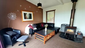 Ein Wohnzimmer mit schwarzem Ledersofa, einem Holztisch, einem schwarzen Hocker, einem gerahmten Bild an der Wand und einem Kaminofen.