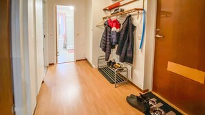 A hallway with a shoe rack, a coat rack with clothes, and a door.