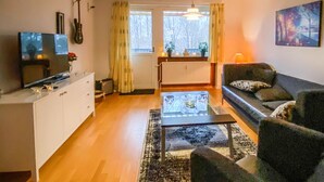 A living room with a sofa, a coffee table, a TV, and a guitar on the wall.