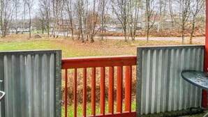 A view from a covered outdoor area with a red railing, a metal table, and a grassy area with trees and houses in the background.