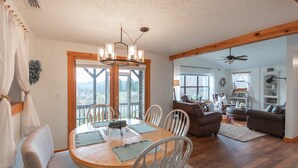 A dining area with a wooden table and white chairs, a chandelier, and a view of the outdoors.