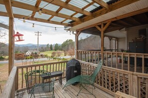 A wooden deck with a covered area, outdoor furniture, and a grill.