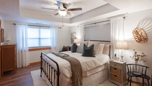 A bedroom with a bed, bedside tables, a chair, a ceiling fan, and a window.