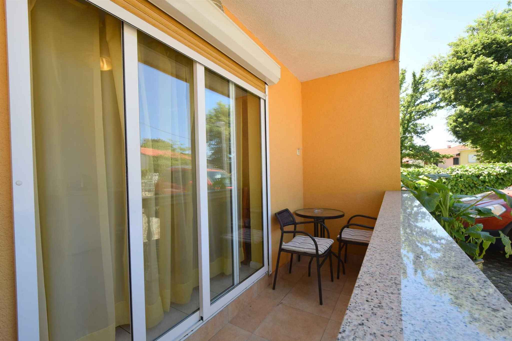 A balcony with a sliding glass door, a small round table, two chairs, and a tiled floor.