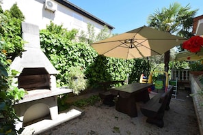 An outdoor patio with a stone barbecue grill, a wooden table, and a large umbrella providing shade.