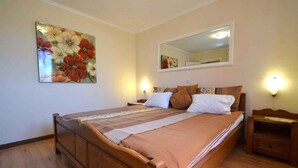 A bedroom with a wooden bed, a large floral painting, a mirror, and bedside lamps.