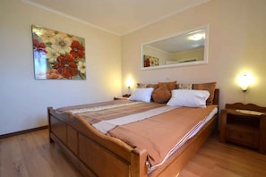 A bedroom with a wooden bed, a large floral painting, a mirror, and bedside lamps.