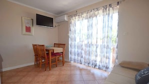 A dining area with a table and chairs, a TV mounted on the wall, and a window with patterned curtains.