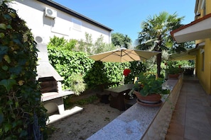 A patio with a table and chairs, surrounded by greenery and a building.