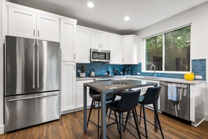 A modern kitchen with white cabinets, stainless steel appliances, a blue backsplash, and a large window.