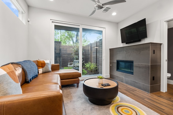 A modern living room with a leather sofa, a round coffee table, and a flat-screen TV mounted on the wall.