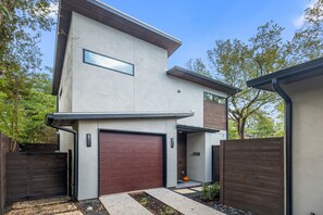 A modern two-story house with a garage, a wooden fence, and a small garden area with a pumpkin.