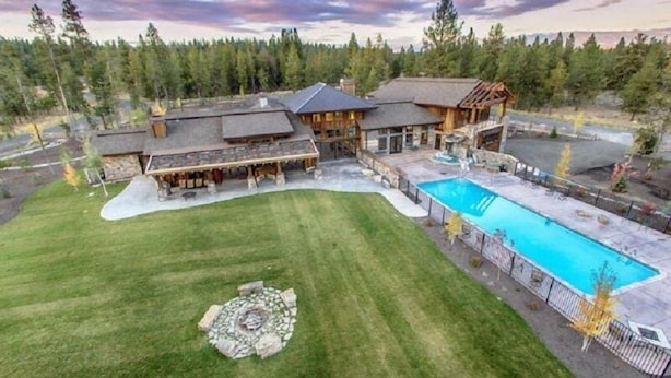 Una casa grande con piscina, una zona de fogata y un césped bien cuidado.