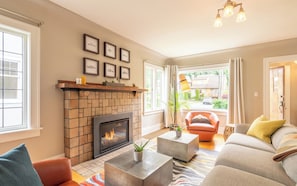 A living room with a fireplace, a sofa, a coffee table, and a view of the outside.