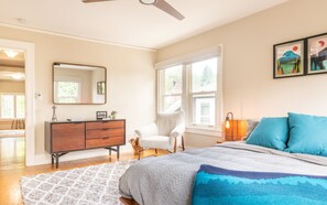 A bedroom with a bed, dresser, chair, and artwork on the wall.