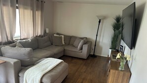 Una sala de estar moderna con un sofá modular, una mesa de centro, una lámpara de pie y un televisor de pantalla plana montado en la pared.