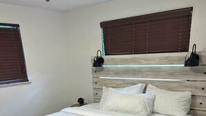 Una cama bien hecha con sábanas blancas y una toalla verde, un cabecero de madera y una ventana con persianas.